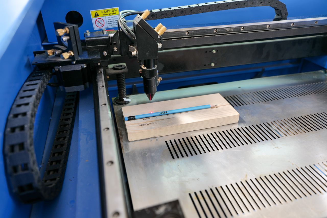 services-01 Laser engraving machine in action on wood with pencil for precise marking.